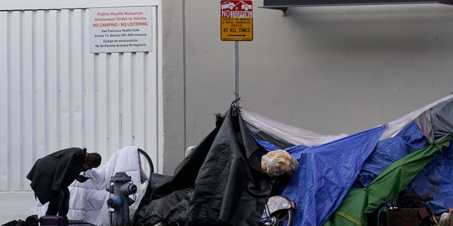 FILE - A man stands near tents on a sidewalk in San Francisco, Nov. 21, 2020. Advocates for homeless people sued the city of San Francisco, Tuesday, Sept. 27, 2022, demanding that it stop harassing and destroying belongings of people living on the streets and commit to spending $4 billion for affordable housing. (AP Photo/Jeff Chiu, File)