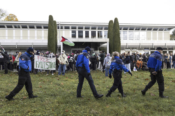 Police walk past protesters holding up placards on the situation of the Israel-Hamas war during a demonstration during the visit of French President Emmanuel Macron and Swiss President Alain Berset to the University of Lausanne (UNIL), Switzerland, Thursday, November 16, 2023.